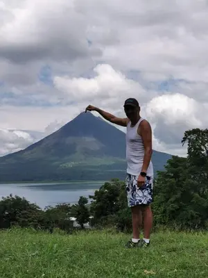 a man standing on a hill looking at a mountain at Sunset Inn Arenal B&B in Fortuna