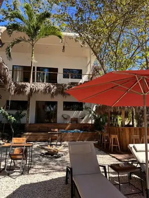 a patio with a red umbrella and chairs and a building at La Sana Surf Hotel, Playa Carmen in Santa Teresa Beach