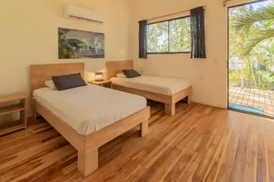 two beds in a room with wooden floors and windows at La Sana Surf Hotel, Playa Carmen in Santa Teresa Beach