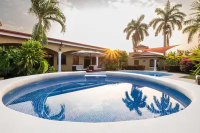 a swimming pool in front of a house with palm trees at Las Brisas Resort and Villas in Jacó