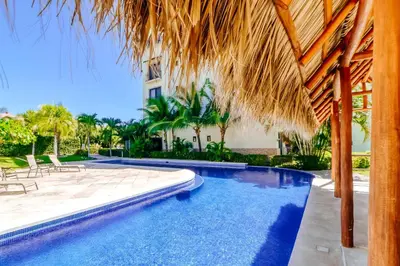 a resort swimming pool with a straw umbrella at Oceanica 804 in Playa Flamingo