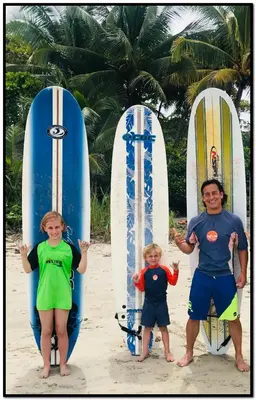 a man and two children standing next to surfboards on the beach at Beach Break Santa Teresa Apartamentos in Santa Teresa Beach