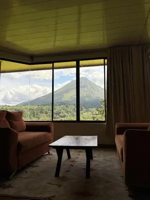 a living room with a table in front of a large window at Arenal Roca Lodge & Bungalows in Fortuna