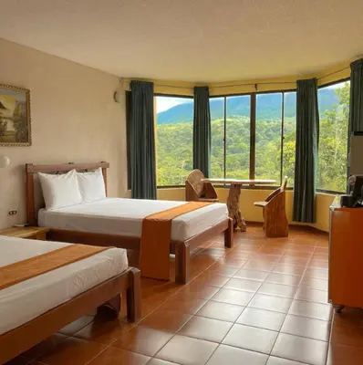 a hotel room with two beds and a large window at Arenal Roca Lodge & Bungalows in Fortuna
