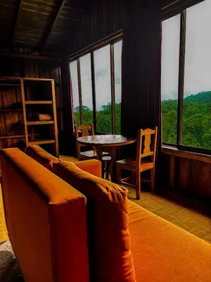 a living room with a table and chairs and windows at Arenal Roca Lodge & Bungalows in Fortuna