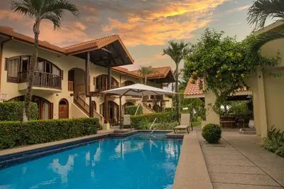 a villa with a swimming pool in front of a house at Apartotel Girasol in Jacó