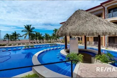 a resort with a large swimming pool with a straw umbrella at 777J Beachfront Luxury Condo 3 BR/2.5BA Near SJO - Jaco Beach in Jacó