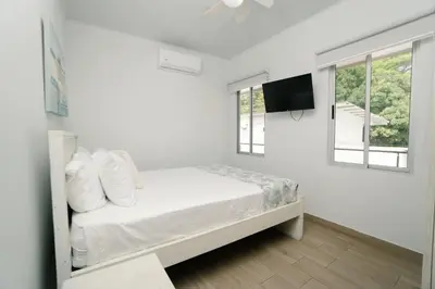 a white bedroom with a bed and a flat screen tv at Apartamentos Ganesha Jacó in Jacó