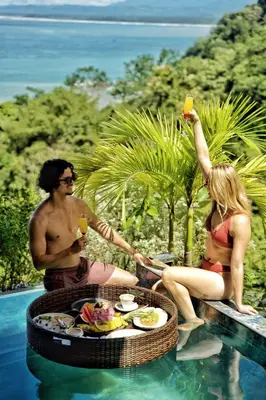 a man and woman sitting next to a pool with drinks at Makanda by The Sea Hotel Adults Only in Manuel Antonio