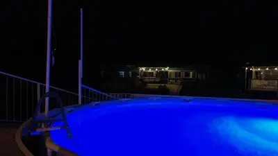 a blue swimming pool at night with houses in the background at Combi Bus Dreamcatcher in Sarchí