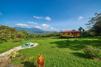 a house in the middle of a grass field with a surfboard at Beautiful 2 Bedroom Villa with Private Nature Reserve - Friendship House in Bijagua