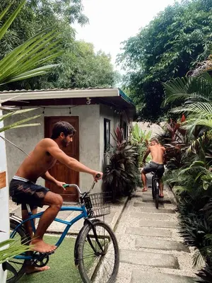 two men riding bikes in front of a house at Cabinas Playa Surf Hostel in Santa Teresa Beach