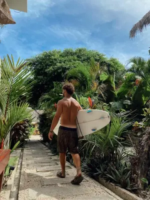 a man walking down a path holding a surfboard at Cabinas Playa Surf Hostel in Santa Teresa Beach