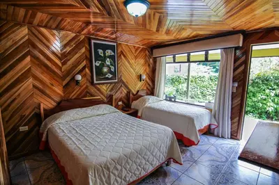 two beds in a room with wooden walls at Hotel Don Taco in Monteverde Costa Rica