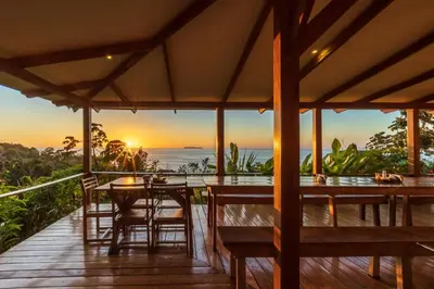 a wooden deck with a table and chairs and the sunset at Punta Marenco Lodge in Drake