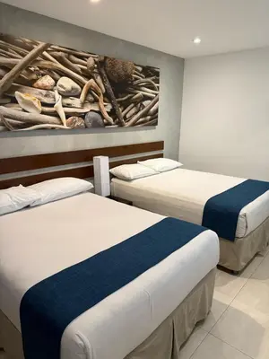 two beds in a room with a painting on the wall at Isla Verde Hotel in San José