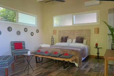 a bedroom with a bed and two chairs and windows at Funky Monkey Lodge in Santa Teresa Beach
