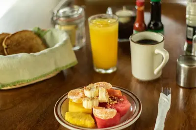 a plate of fruit on a wooden table with orange juice at Cabinas Las Olas in Playa Avellana
