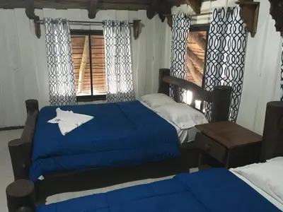 a bedroom with two beds with blue sheets and a window at Hotel Samsara in Uvita