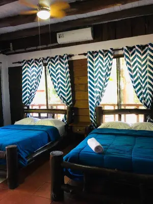 two beds in a room with blue sheets and windows at Hotel Samsara in Uvita