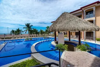 a resort with a large swimming pool with a straw umbrella at Beautiful and Enchanting Beach Vacation in Jacó