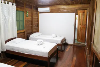 two beds in a room with wooden walls and wood floors at Hotel La Cascada in Puntarenas