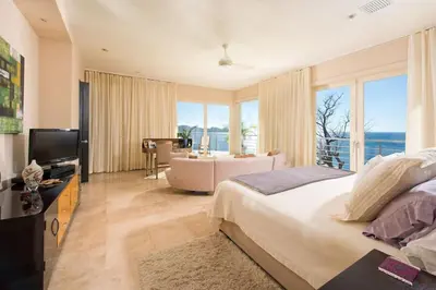 a bedroom with a large bed and a living room at Exquisite Hilltop Villa with Luxurious Modern Design, Sweeping Ocean Views & Sparkling Infinity Pool in Playa Flamingo