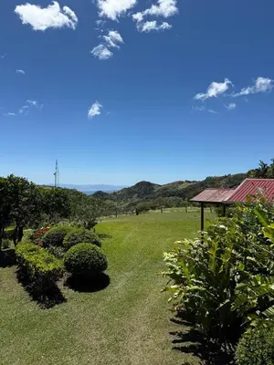 a field with bushes and a house with a blue sky at Campo Azul #2 - Monteverde in Monteverde Costa Rica