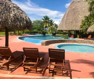 two chairs and a swimming pool with a straw umbrella at Nandel Beach Resort in La Cruz