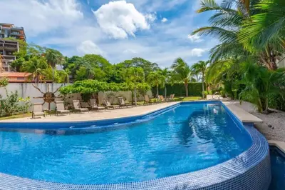 a swimming pool with chairs and palm trees at Elegant Oceanview Condo with Spacious Open-Concept Floor Plan and Inviting Beach Design in Playa Flamingo