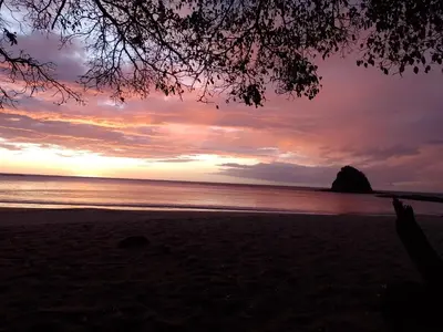a sunset on the beach with a rock in the distance at Nasu Lodge in La Cruz