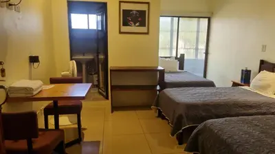a room with two beds and a table and a desk at Hotel la Cueva Limon in Puerto Limón