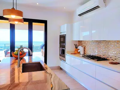 a kitchen with white cabinets and a view of the ocean at Casa de Iluminacion - Gorgeous 5-BR oceanview Villa with private infinity Pool in Brasilito