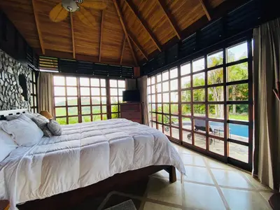 a bedroom with a large bed and large windows at Tropical Balinese Villa Atenas in Escobal