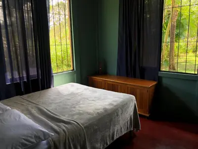 a bedroom with a bed and two large windows at Casita el jardin in Bijagua