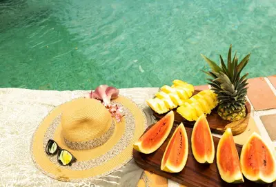a straw hat and a plate of fruit next to a pool at Hotel El Rancho in Quepos