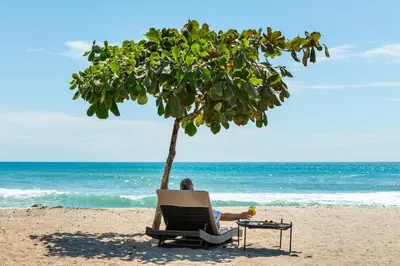 a man sitting in a chair under a tree on the beach at Luxury Beachfront Villa with private pool at Nantipa in Santa Teresa Beach