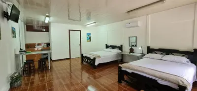 a bedroom with two beds and a table and a kitchen at Sleep&Go! Cabina Cuadruple en Siquirres Centro - and rafting tour! in Siquirres