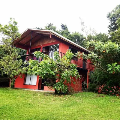 a red house with a balcony in the grass at Casa de Montaña Tica Linda in Monteverde Costa Rica