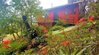 a red house with red flowers in front of it at Casa de Montaña Tica Linda in Monteverde Costa Rica