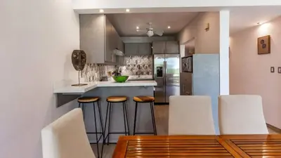 a kitchen with white chairs and a wooden table at Elegant Condo with Brand-New Fixtures, Shaded Tropical Terrace, and Secluded Beach Access in Playa Flamingo
