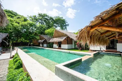 a swimming pool at a resort with a thatched roof at LA QUEBRADA ECO LODGE Hotel Boutique in Potrero
