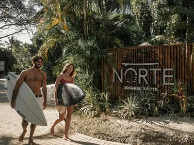 a man and a woman walking down the street with a surfboard at Norte Nosara - Steps to Playa Guiones in Nosara