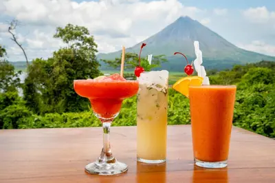 three drinks on a table with a mountain in the background at Villas Paradise Arenal Volcano Lake View in El Castillo de La Fortuna