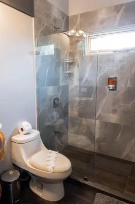 a bathroom with a toilet and a glass shower at Hotel FAREMITI Uvita in Uvita
