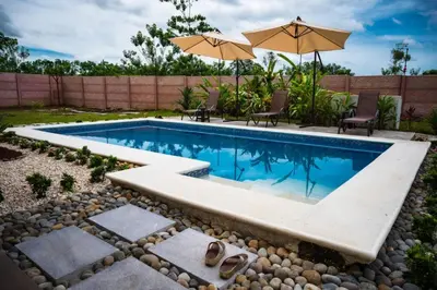a swimming pool in a backyard with chairs and an umbrella at Villa Tropical La Fortuna in Fortuna