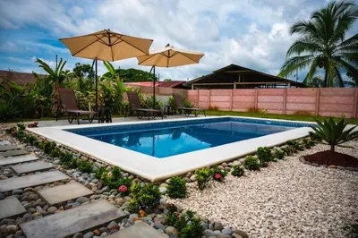 a swimming pool in a garden with two chairs and an umbrella at Villa Tropical La Fortuna in Fortuna