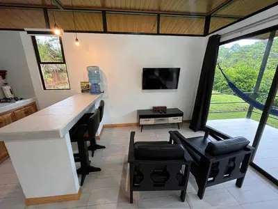 a kitchen with a bar with black chairs and a tv at Pacheco Tours Rainforest Cabins 4x4 Only in Drake