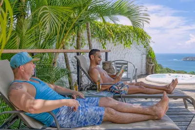 two men are sitting in chairs on the beach at Villa Roca Boutique Resort & Suites - ADULT ONLY in Manuel Antonio