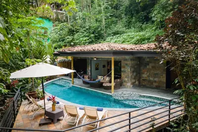 a pool with chairs and an umbrella next to a house at Rainforest Gem Aracari Villa with Private Pool in Quepos